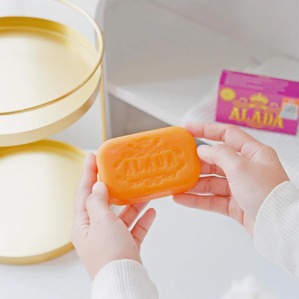 Orange soap bar with 'ALADA' branding held by hands, with a blurred background