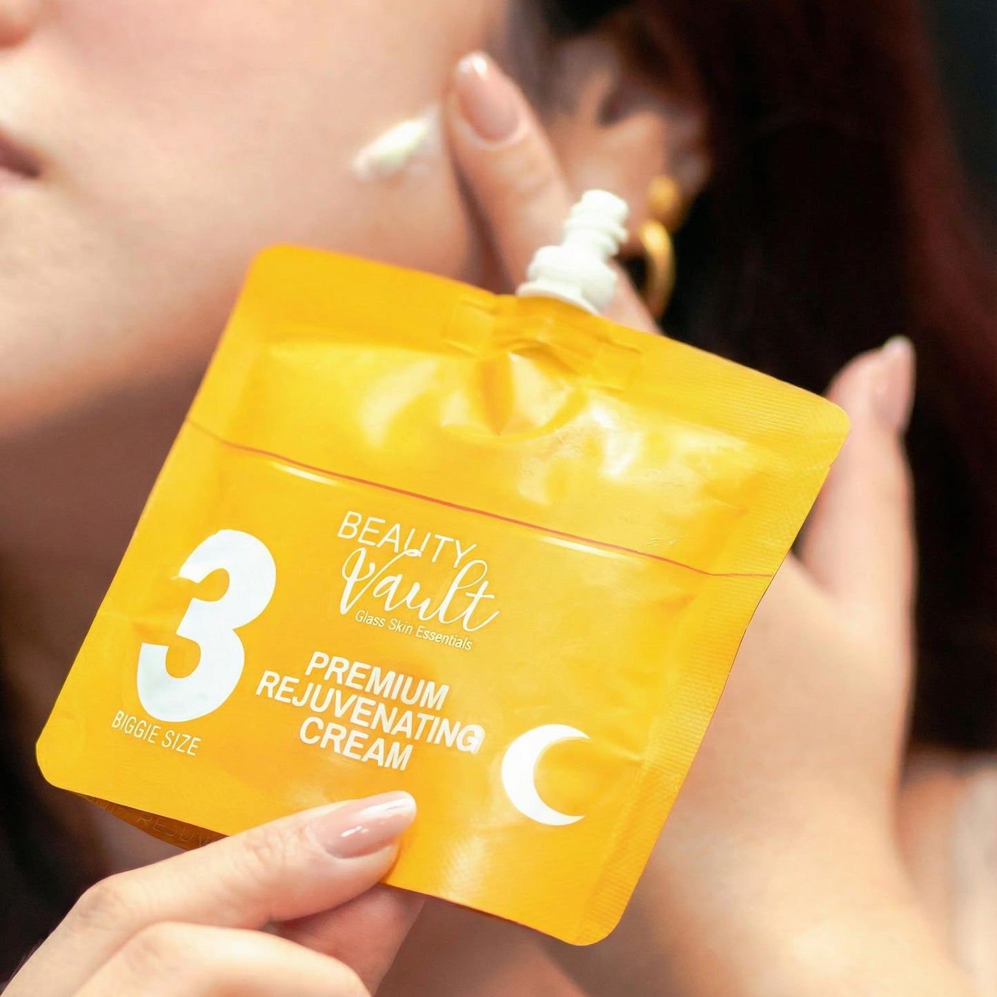 Person holding a yellow packaging of 'Beauty Vault' premium rejuvenating cream.