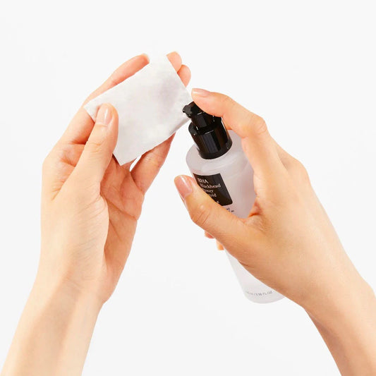 Hands holding a white bottle with a black cap and a white cloth on a light gray background