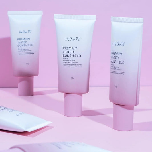 Three tubes of 'her Choice Ph' Premium Tinted Sunshield on a pink background