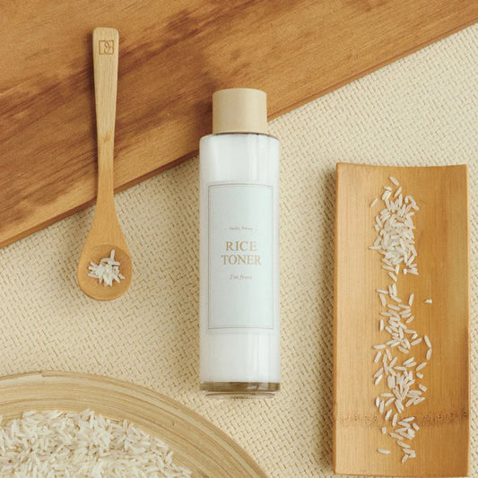 Bottle of rice toner with wooden spoon and rice on a textured surface