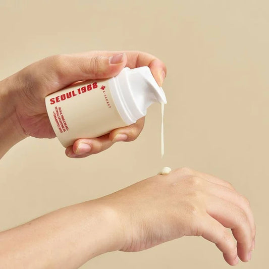 Hand holding a 'SEOUL1988' skincare product with cream being applied to a wrist on a beige background