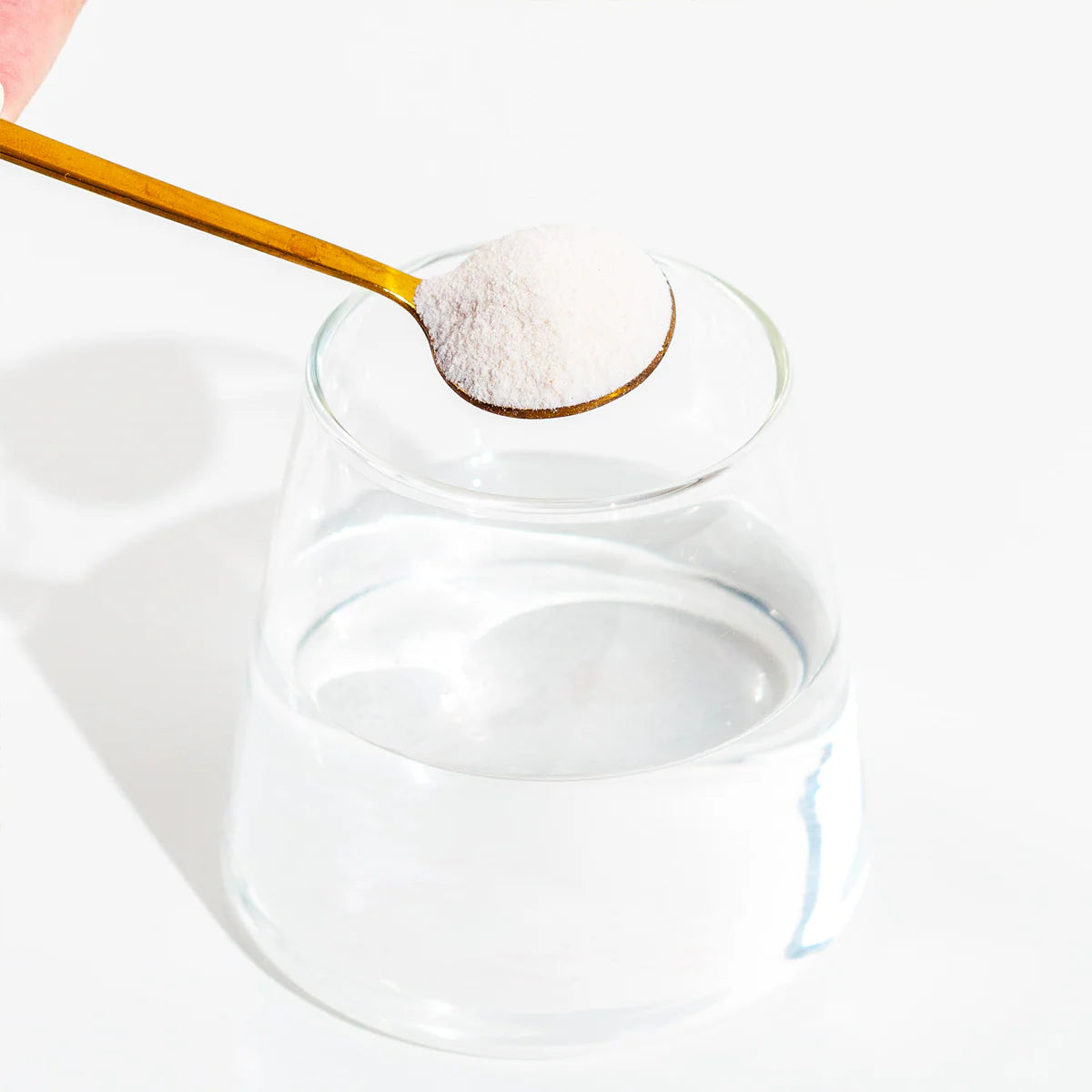 Glass container with a wooden spoon holding white powder above it on a white background