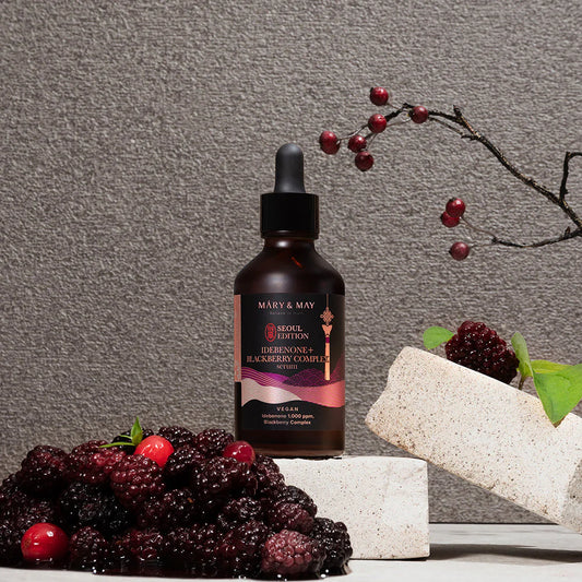 Bottle of Mary & May skincare serum with blackberries and a branch on a gray background