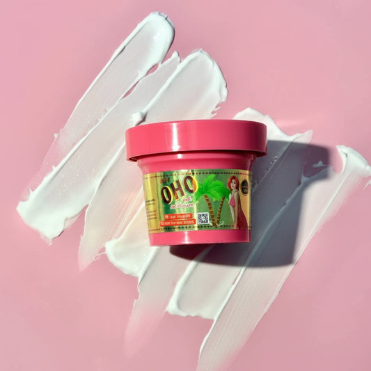 A small jar of OHO hair product with a pink lid and green/yellow label, placed on a pink background with white cream smears behind it.