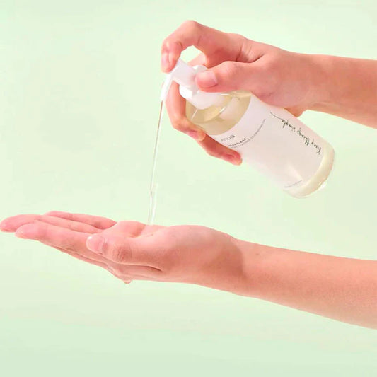 Person holding a bottle of skincare product over another hand against a light green background