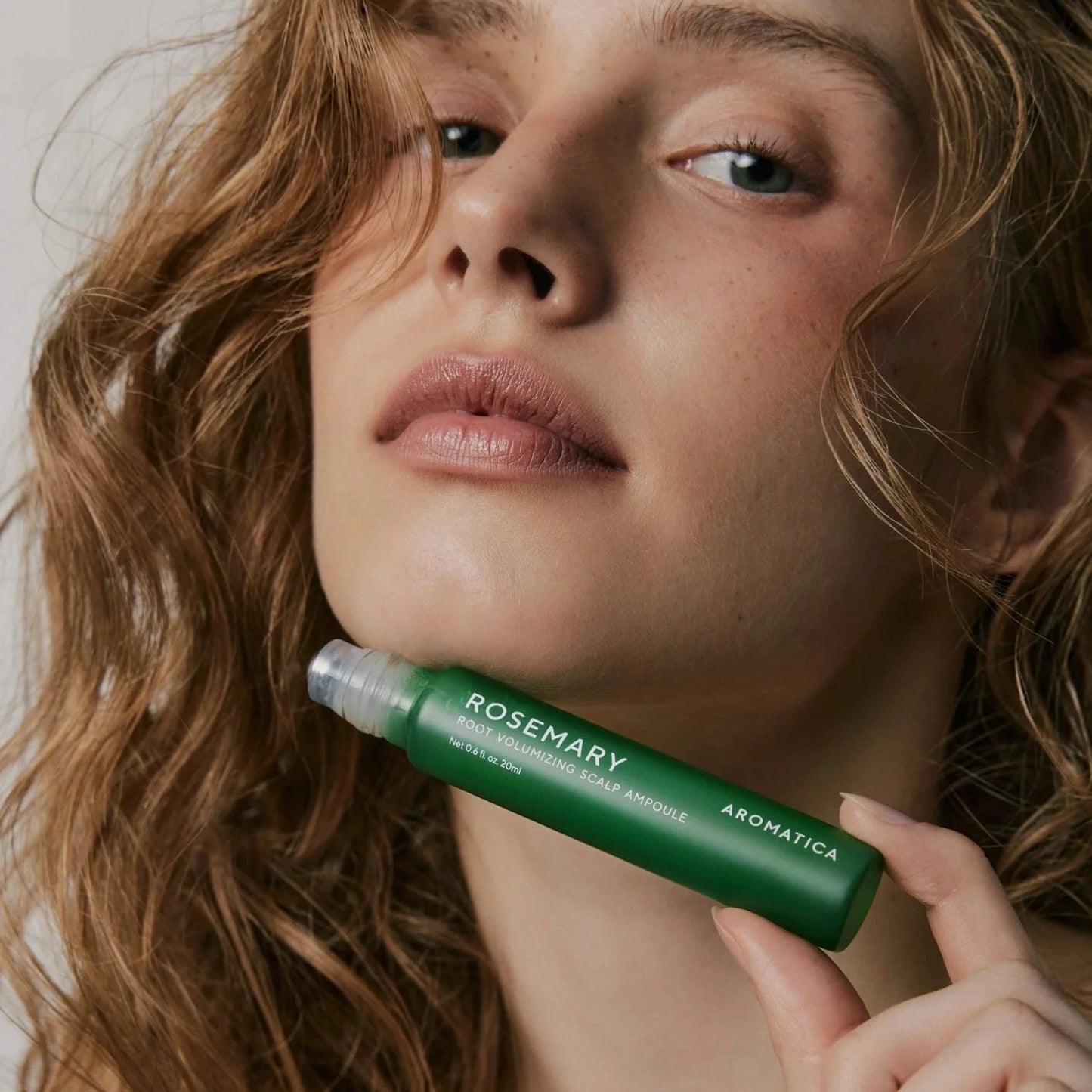Woman holding a green skincare product with visible branding.