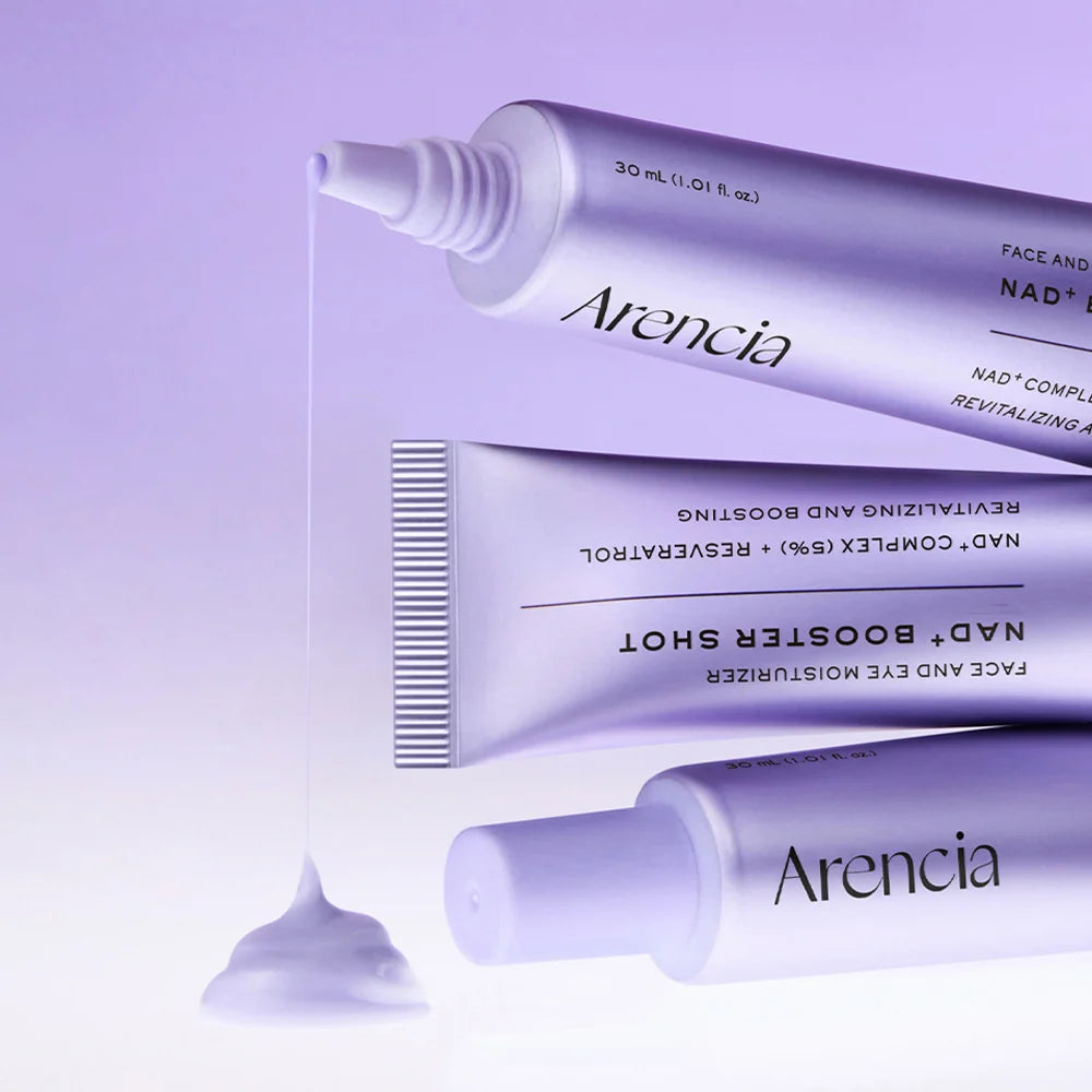 Three lavender tubes of Arencia skincare, including Face and Eye Moisturizer and NAD+ Booster Shot, arranged on a light purple background with a dollop of cream in front.