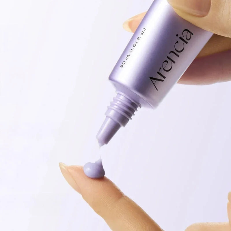 A close-up of a hand squeezing a lavender-purple tube of Arencia cosmetic cream onto another finger, showing the product texture against a clean white background.
