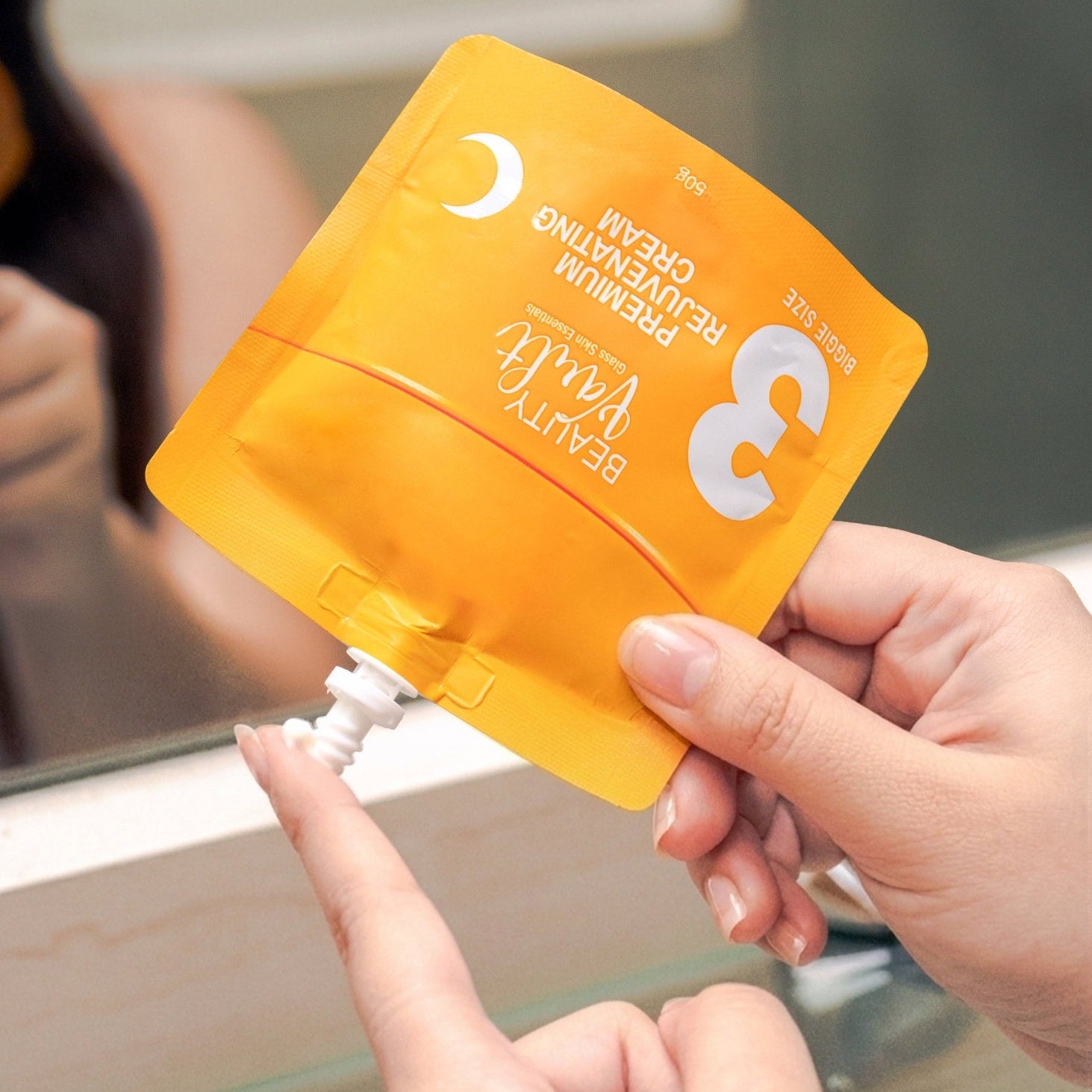 Person holding a yellow skincare product packaging with a mirror in the background