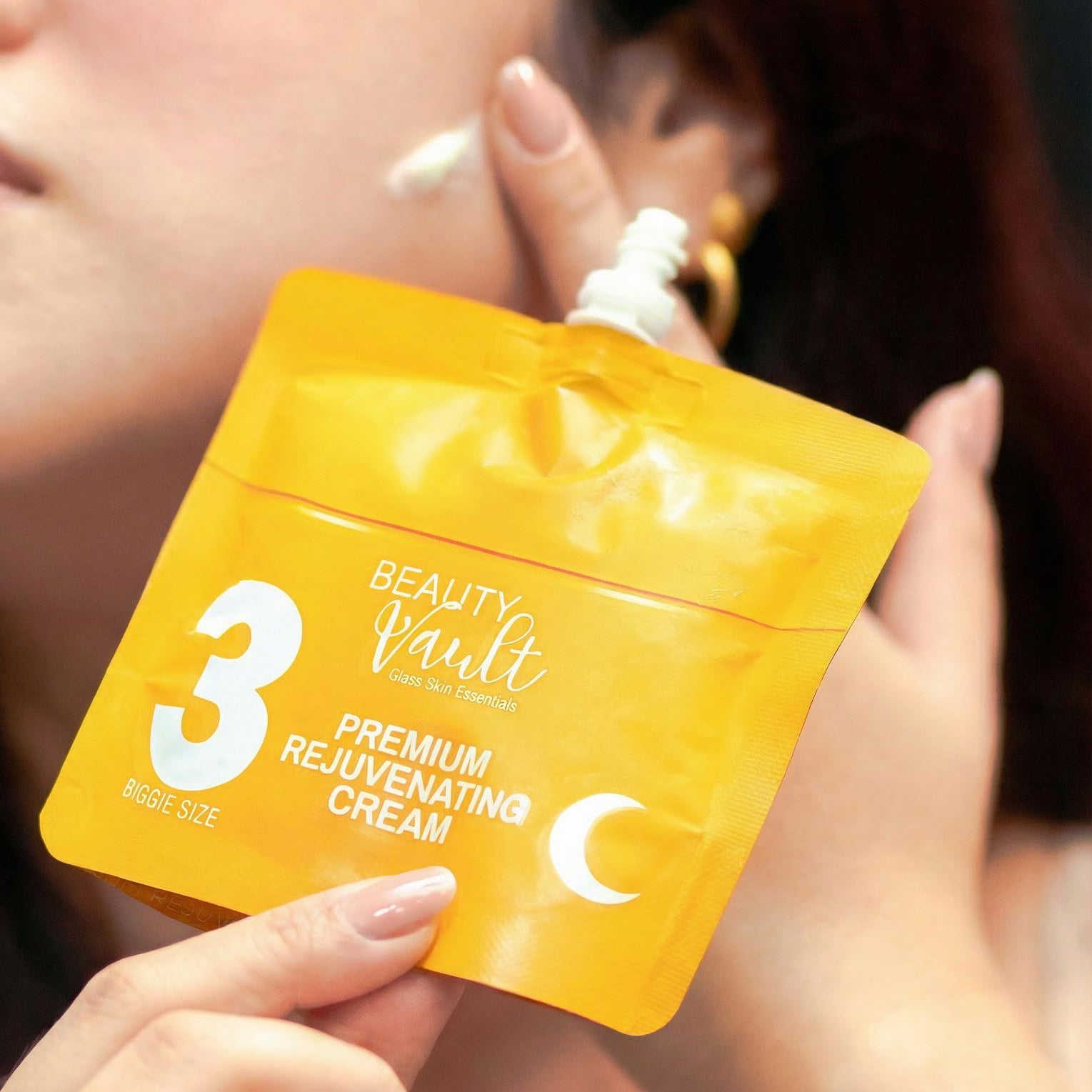 Person holding a yellow packaging of 'Beauty Vault' premium rejuvenating cream.