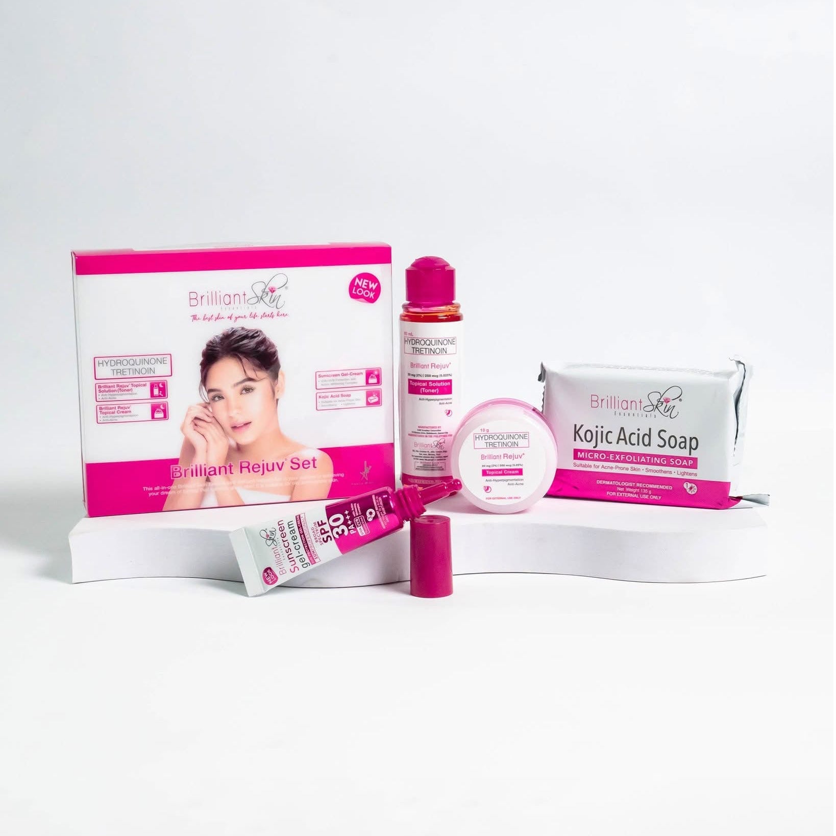 A collection of skin care products including a box of Brilliant Rejuv Topical Cream, a bottle of Brilliant Rejuv Solution, a tube of sunscreen gel-cream, and a bar of Kojic Acid Soap, all displayed on a white background.
