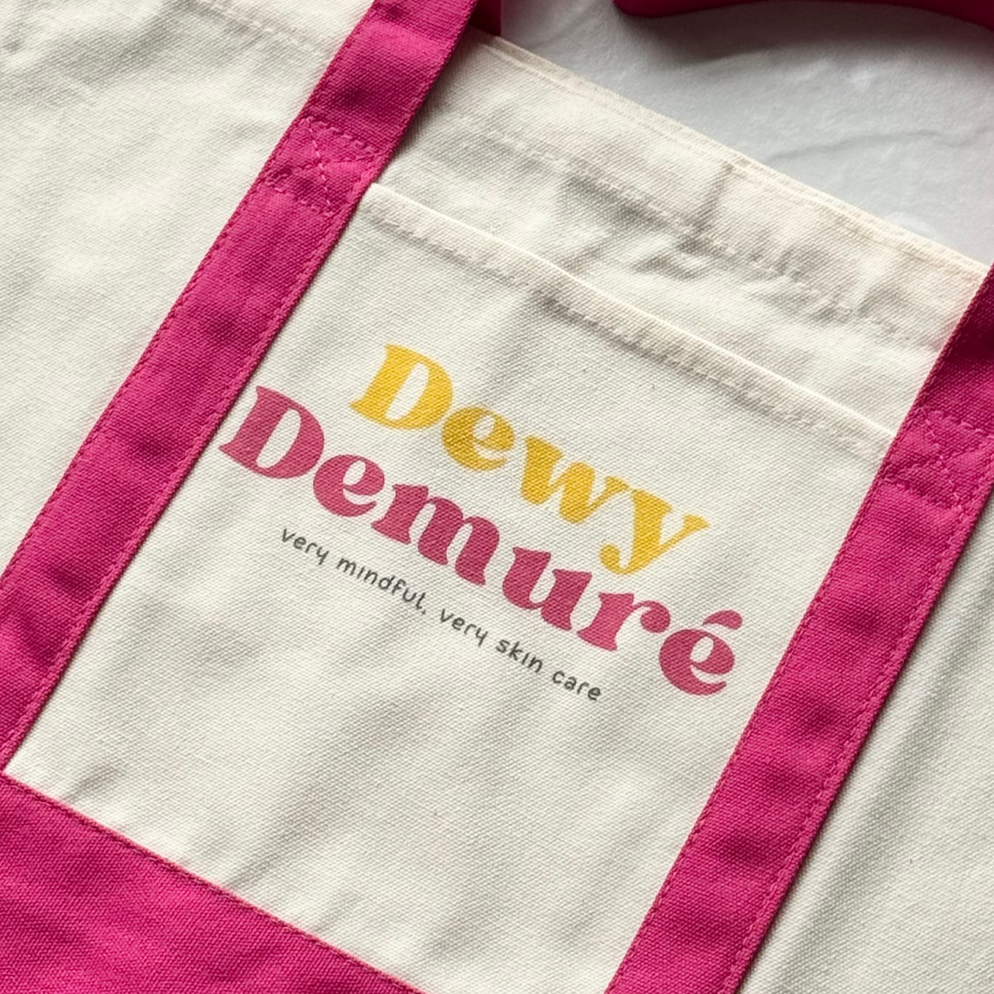 Tote bag with 'Dewy Demure' branding on a light background