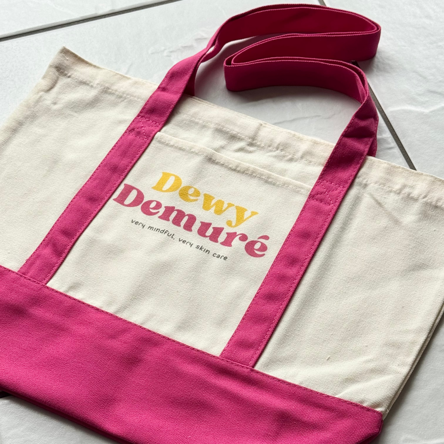 Tote bag with 'Dewy Demure' text on a light gray surface