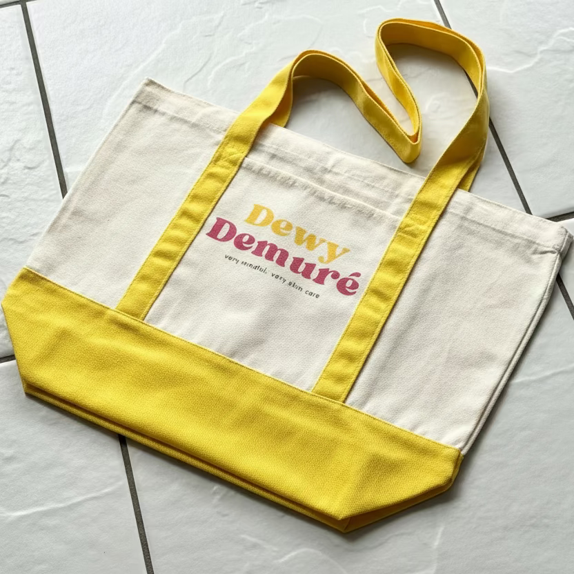 Tote bag with yellow accents and 'Dewy Demure' text on a tiled floor.