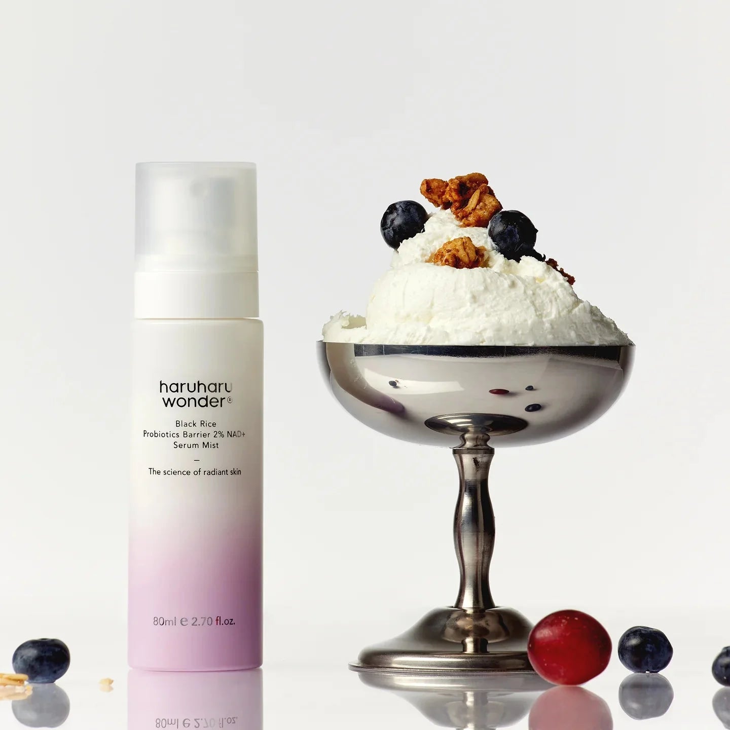 Haruharu wonder skincare product next to a dessert with berries and cream on a reflective surface.