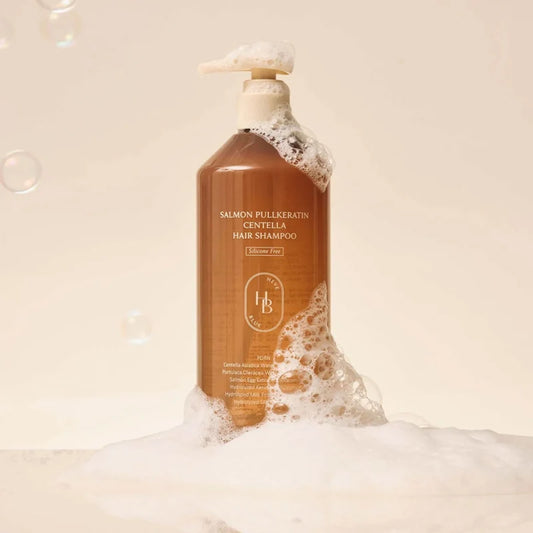 A bottle of salmon-pink pullkeratin gentlla hair shampoo by H&B, shown with white foam and bubbles against a warm beige background.