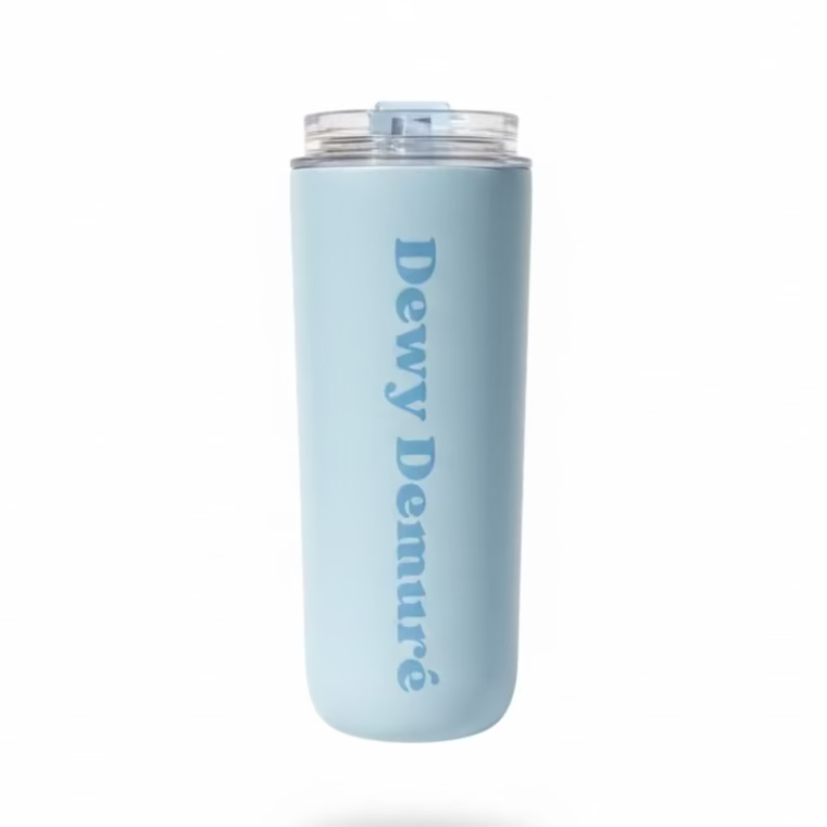 Hand holding a light blue tumbler with 'Dewy Deamure' branding outdoors on grass.