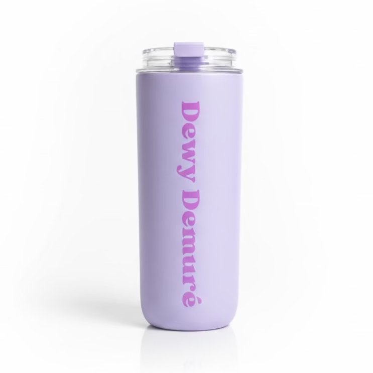 Hand holding a purple tumbler with 'Dewy Demure' text against a green outdoor background