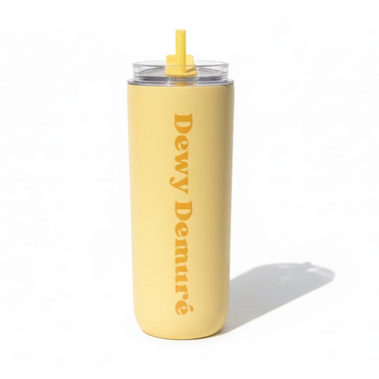 Hand holding a beige tumbler with 'Dewy Demure' text against a grassy outdoor background