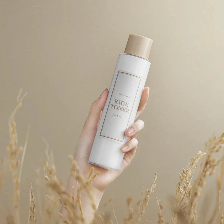 Hand holding a bottle of 'BRIGIT TONER' against a beige background with dry grass.