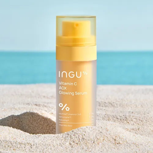 Skincare serum bottle labeled 'INGU' on a sandy beach with ocean view