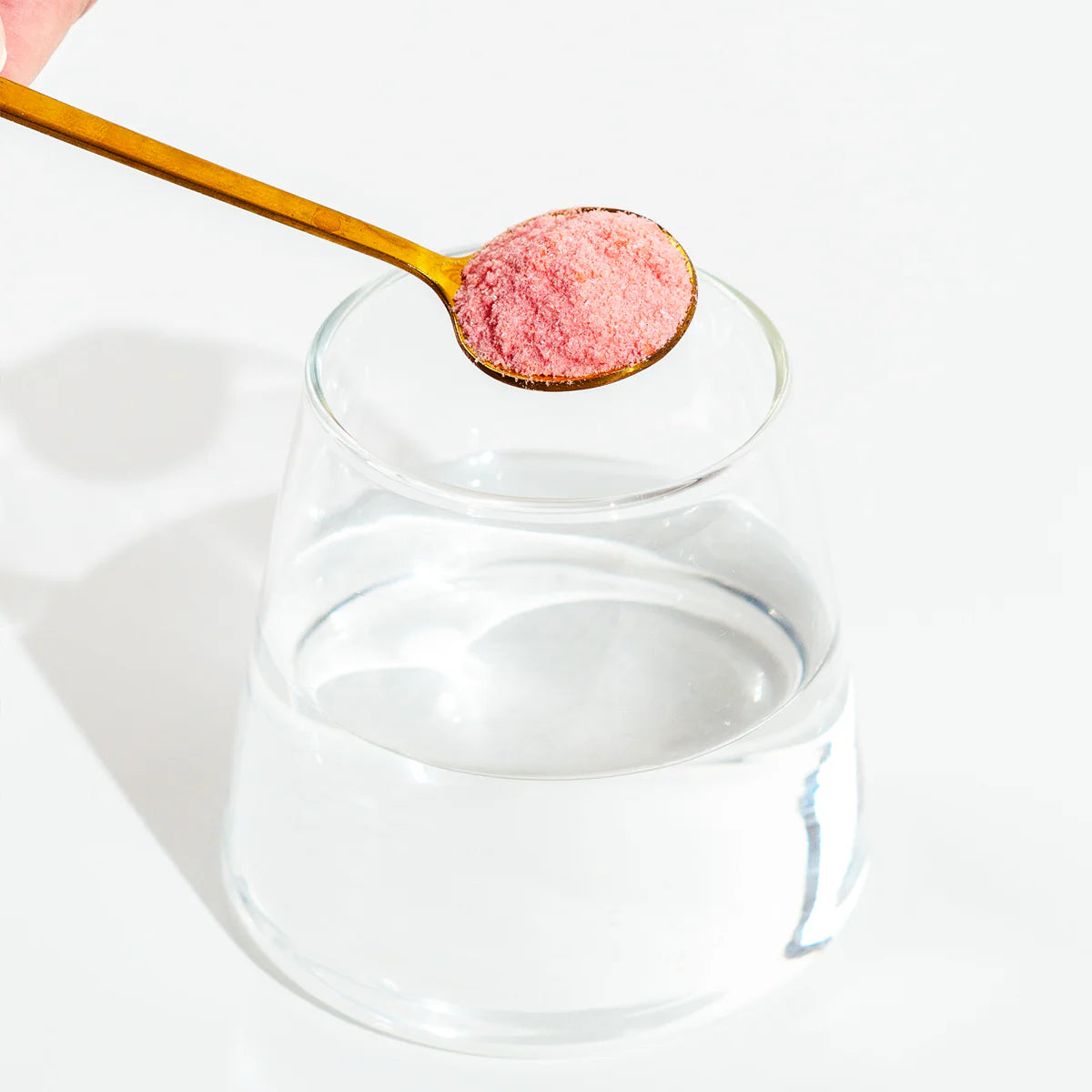 Glass jar with a wooden spoon containing pink powder on a white background