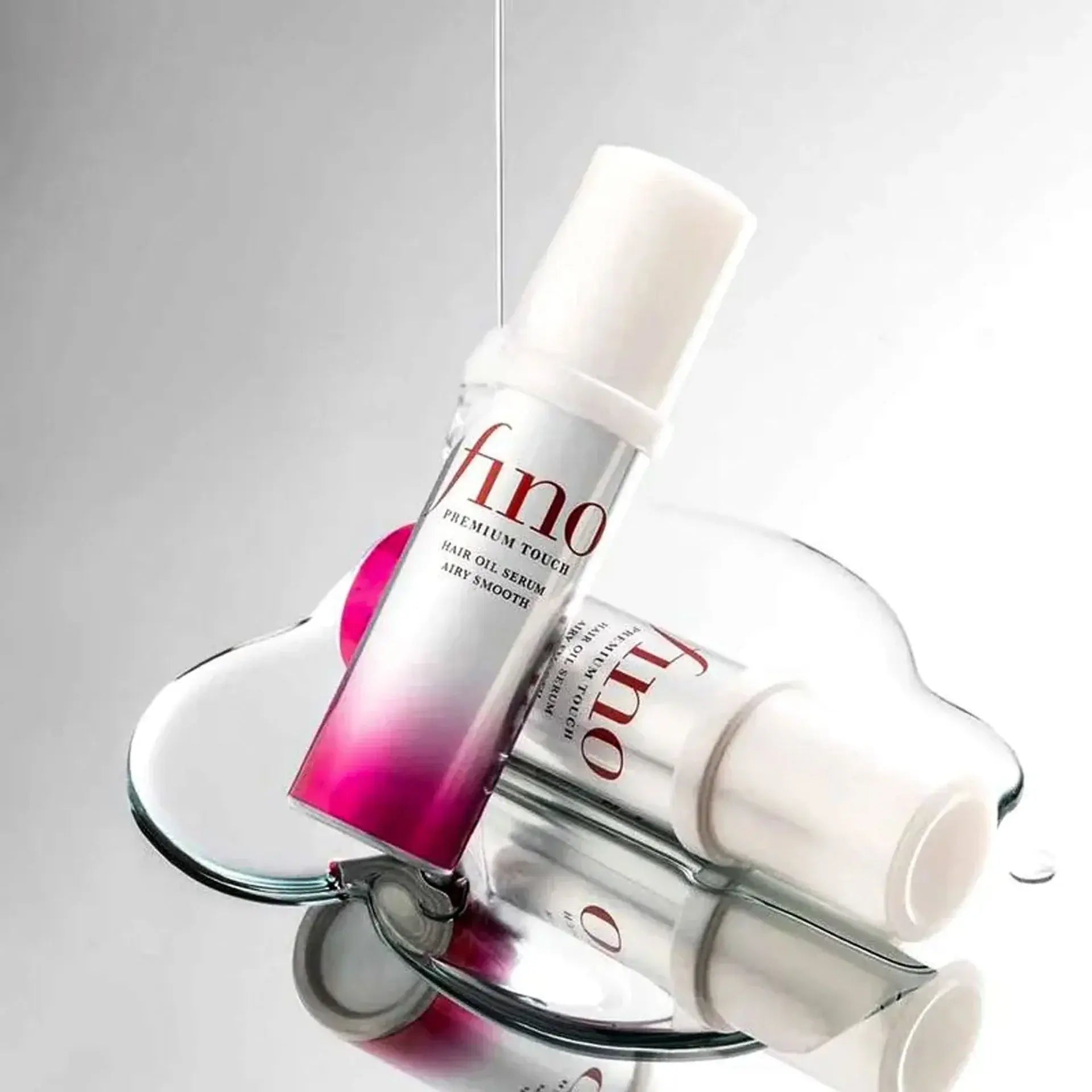 Two bottles of 'fino' hair oil serum on a reflective surface with a gray background