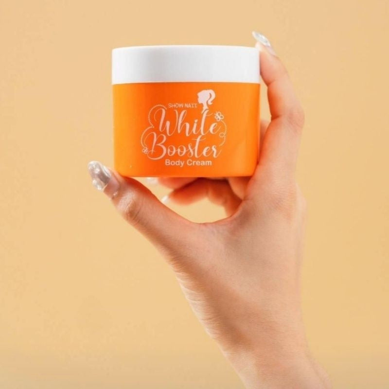 Hand holding an orange container of 'White Booster' body cream against a beige background