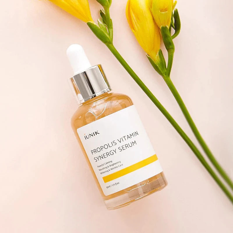 Propolis Vitamin Synergy Serum bottle with yellow flowers on a light pink background