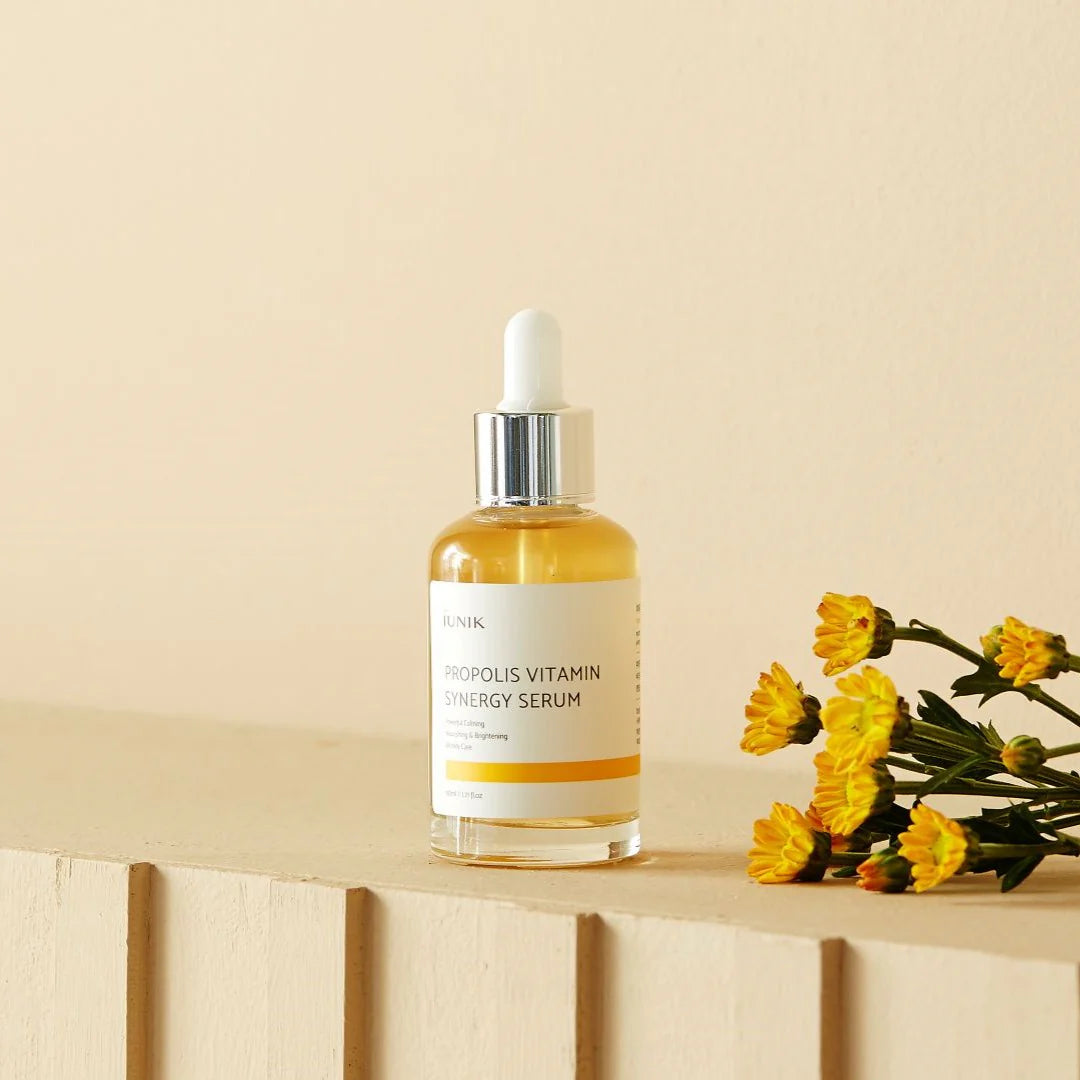 Bottle of Skink Serums Morfolis Vitamin Energy Serum on a wooden surface with yellow flowers.