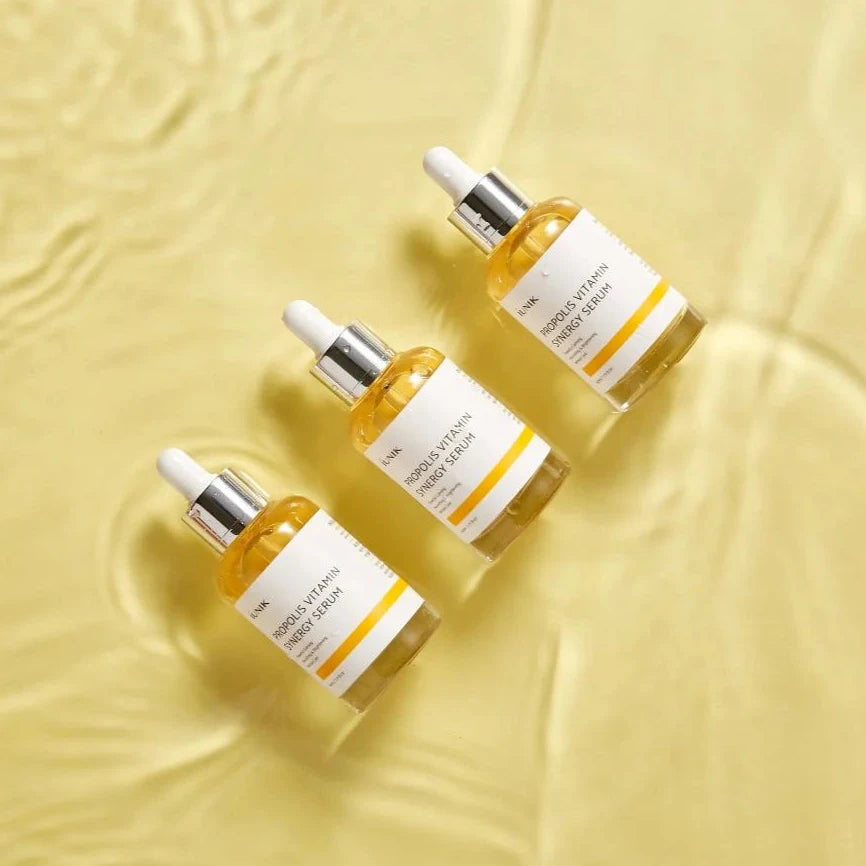 Four skincare serum bottles with droppers on a textured yellow background